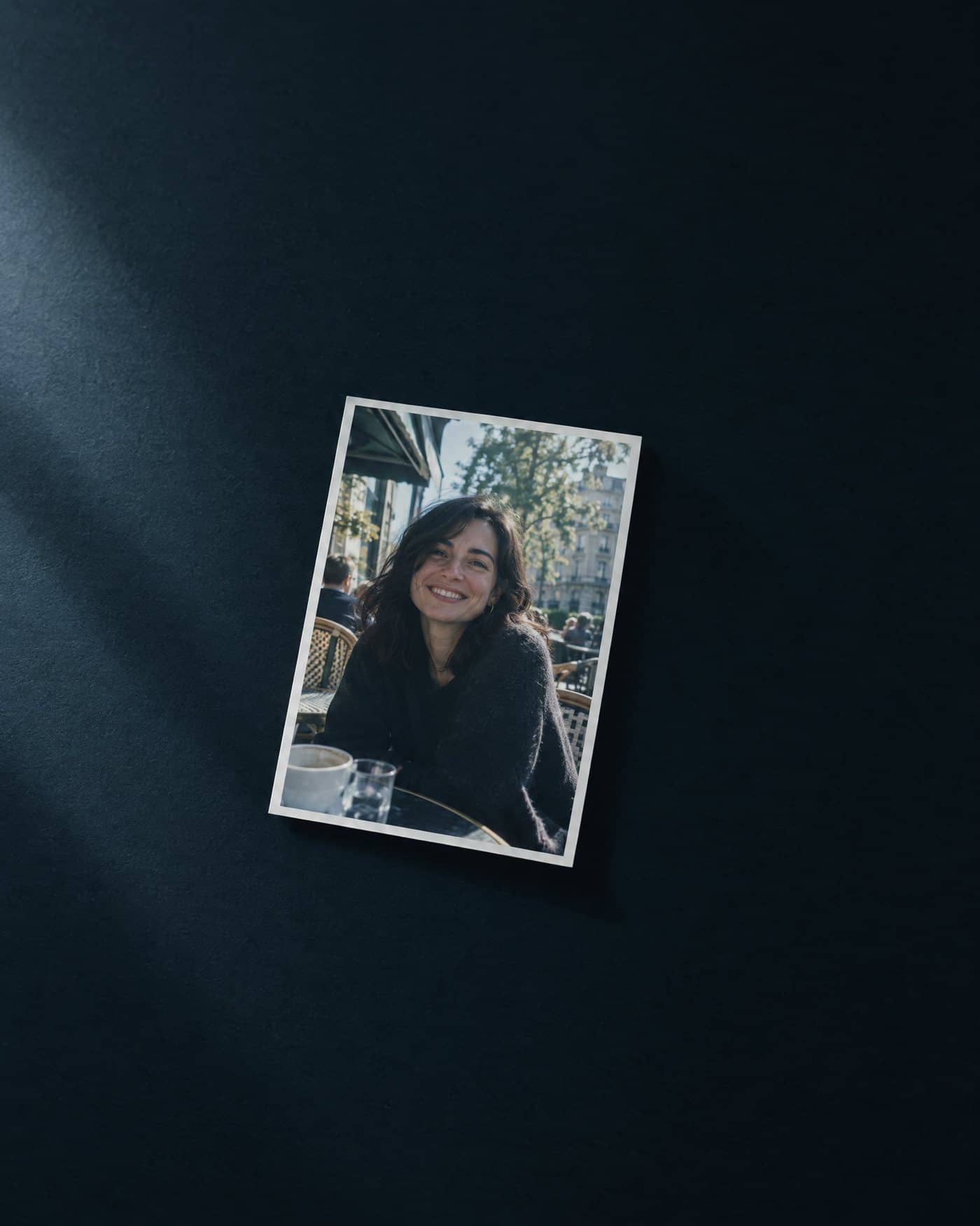 AI-generated image of a printed snapshot lying on a dark desk. The snapshot shows a smiling woman at a cafe table. She is not a real person.